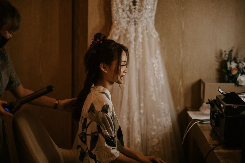 Wedding dress hanging in a warmly lit room with getting ready details.