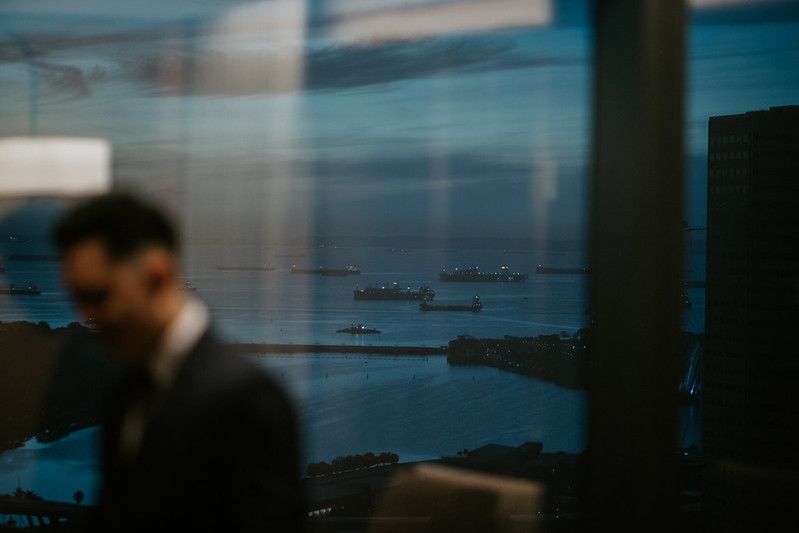 Cityscape view through large windows with ships visible on the water.