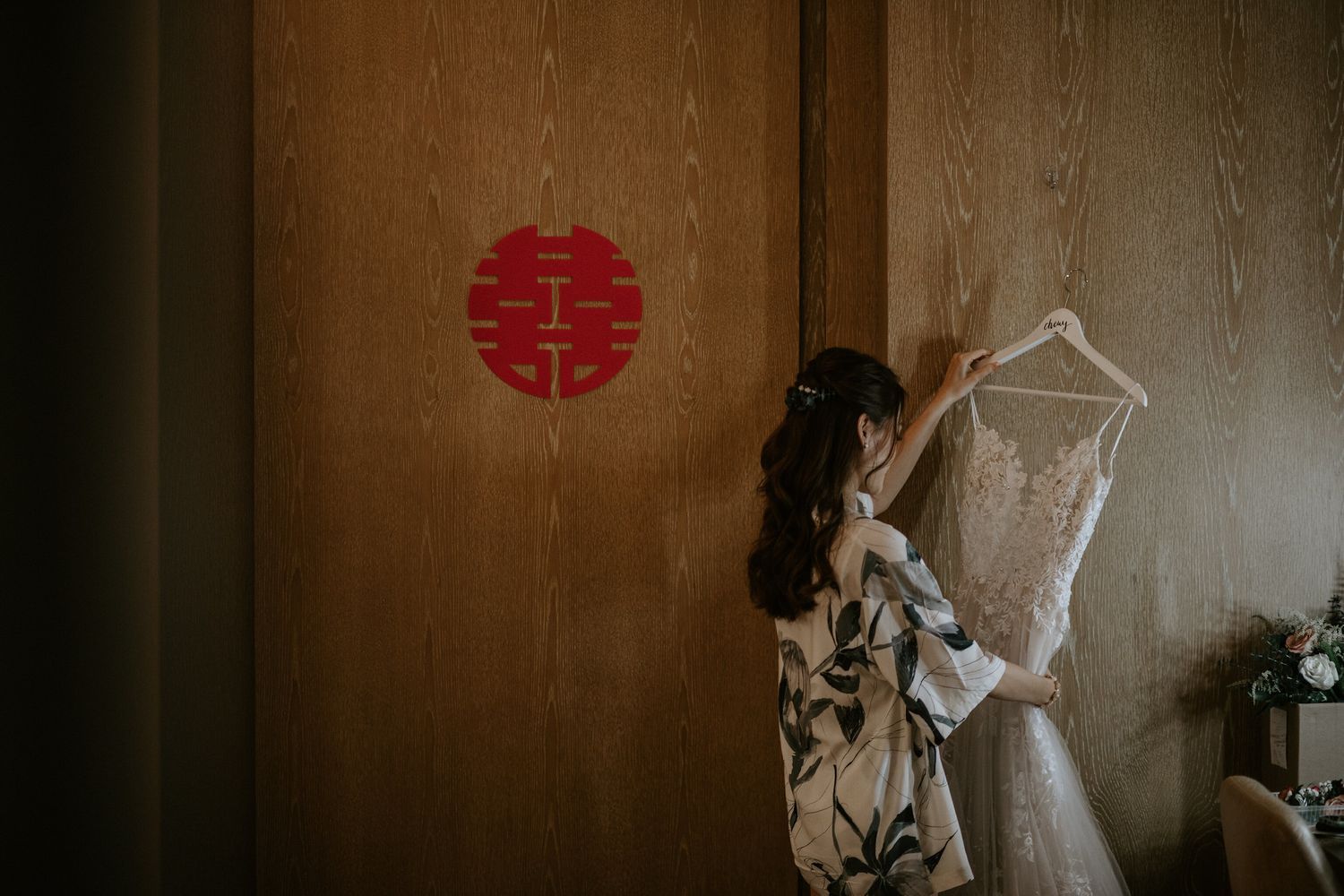 A wedding dress hangs in a room with a red circular design on the wall.