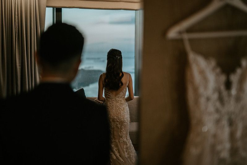 A couple stands silhouetted against large windows with a cloudy sky view.