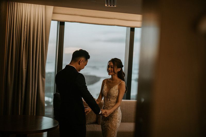 A couple holds hands in an intimate moment by floor-to-ceiling windows.
