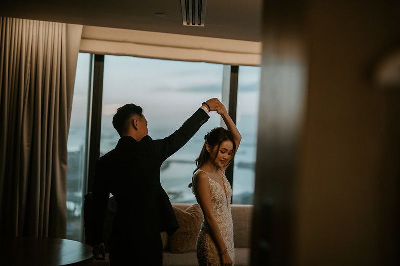 A couple dances together in front of large windows with city views.