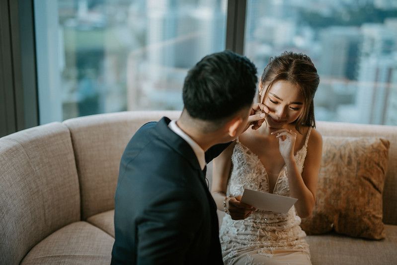 Tender moment between couple on modern sofa with floor-to-ceiling windows.