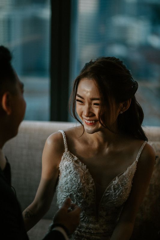 Bride in lace dress smiling while seated on modern grey couch.