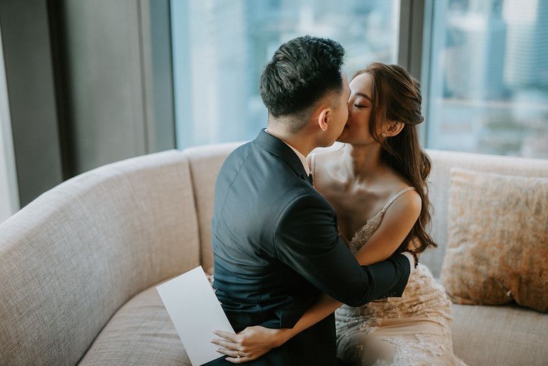 Intimate moment between newlyweds on grey sofa with city views.