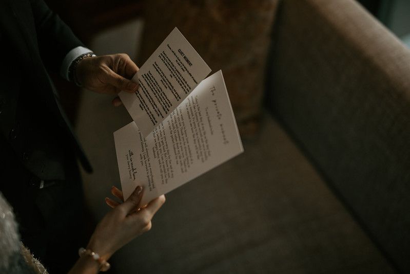 Hands holding a wedding ceremony program or vows document in moody lighting.