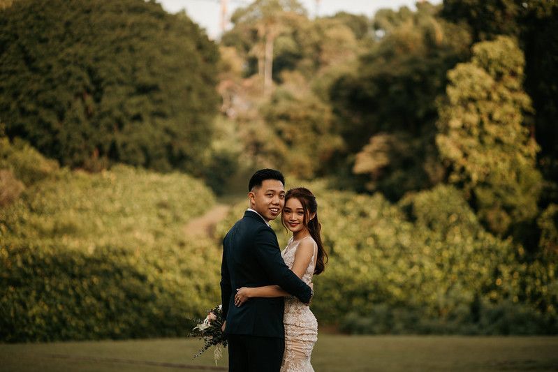 Couple in wedding attire embracing in lush garden setting.