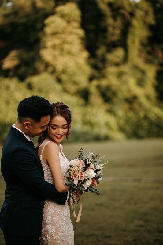 Couple sharing intimate moment with bridal bouquet in outdoor garden setting.