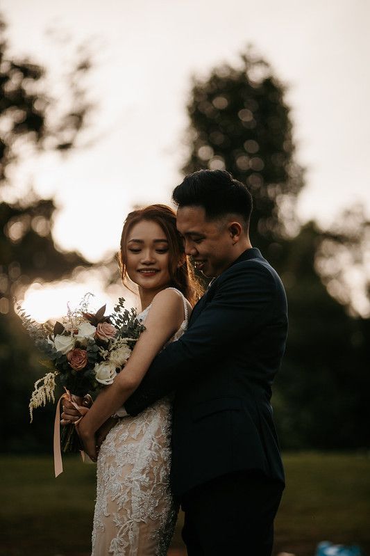 Couple sharing tender moment with floral bouquet in golden hour lighting.