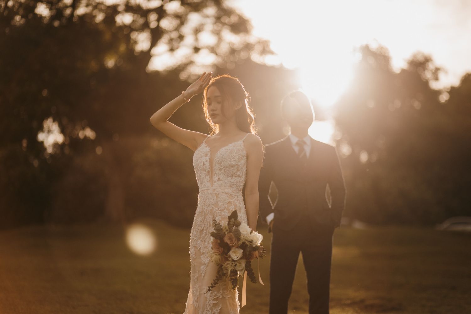 Silhouettes of a wedding couple against a warm sunset backdrop in a park setting.