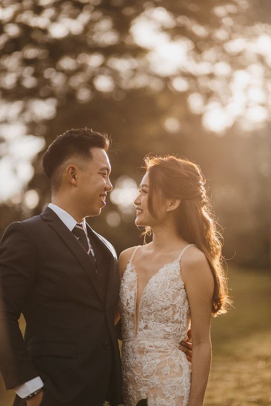 Wedding couple in elegant attire share romantic glances during sunset photo session.