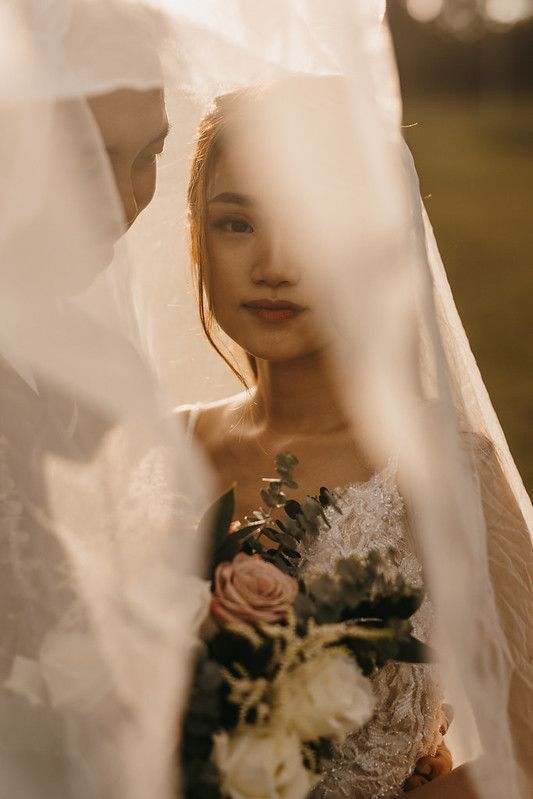 Artistic bridal portrait through sheer veil with delicate floral bouquet details.