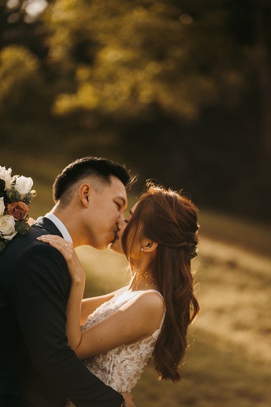 Romantic wedding kiss captured in warm golden sunlight against a natural backdrop.