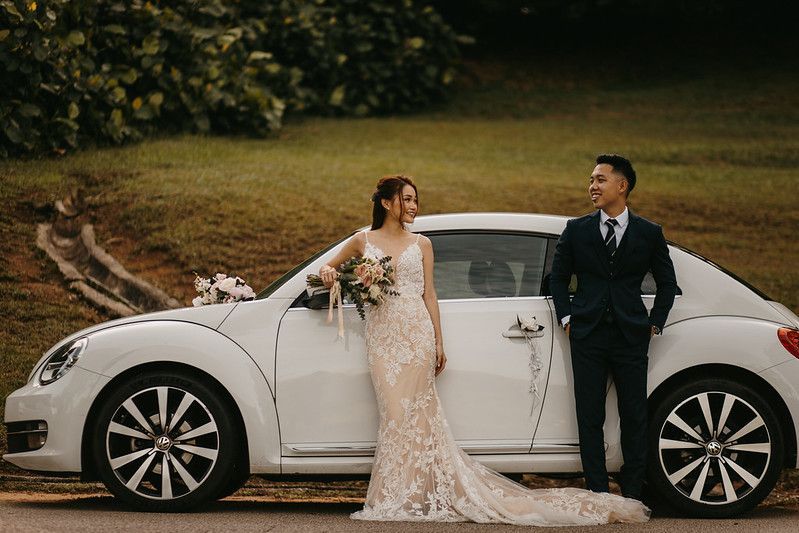 Wedding couple poses elegantly next to a white luxury car in an outdoor setting.