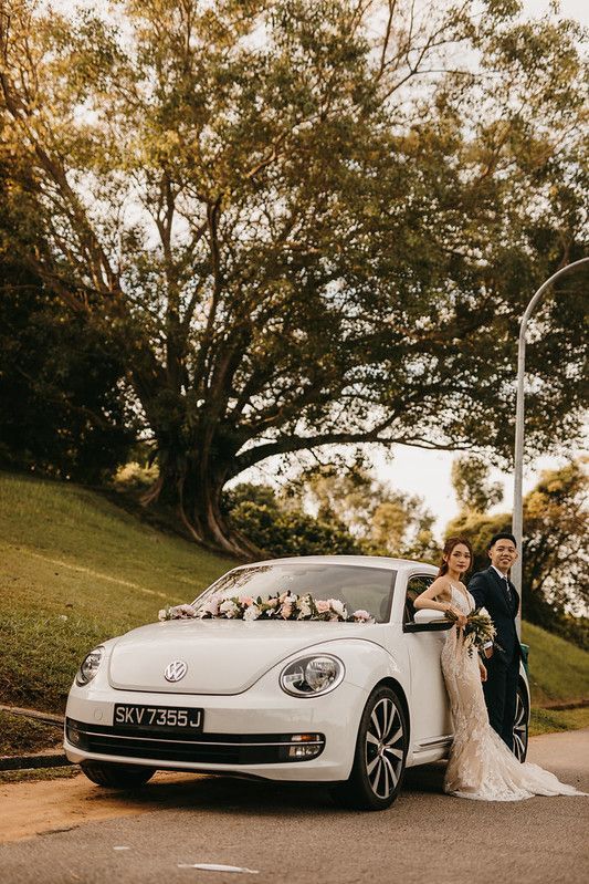 A white Volkswagen Beetle parked under trees during a wedding photoshoot at sunset.