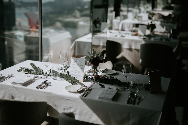 Long banquet tables set with white linens and decorative greenery for an upscale event.