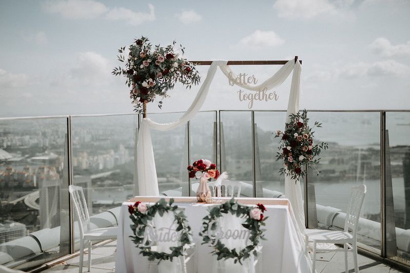 Outdoor wedding ceremony setup on a rooftop terrace with city views and floral arch.