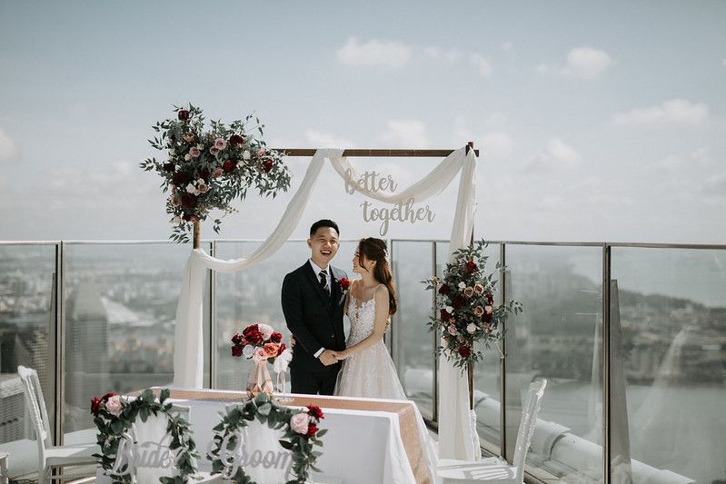 Intimate rooftop wedding ceremony with white fabric arch and floral decorations overlooking the city.