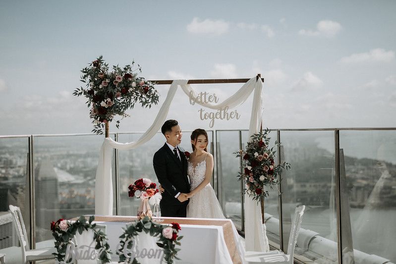Elegant wedding arch decorated with white fabric and flowers on a modern rooftop terrace.