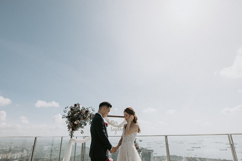 Modern rooftop wedding venue with glass railings and white fabric decorations against an urban skyline.