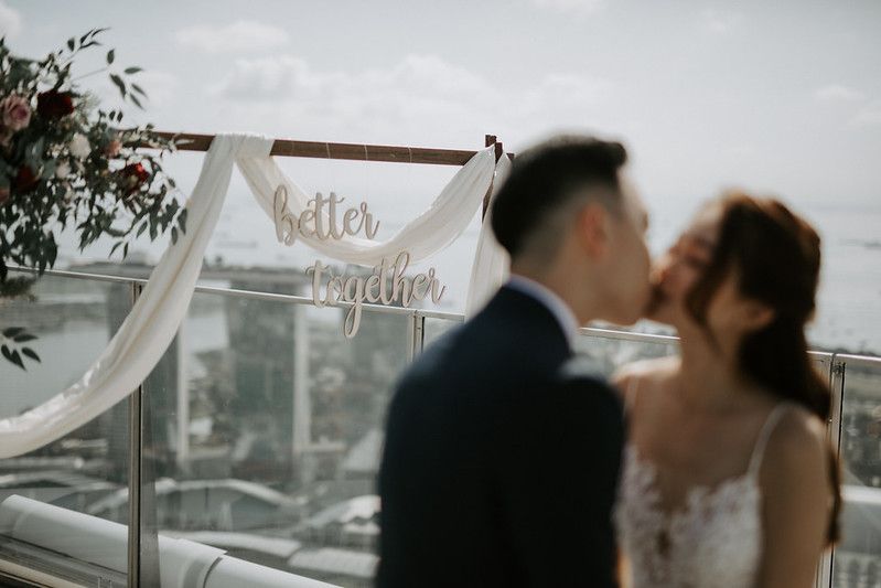 Intimate wedding ceremony moment on a modern rooftop with white fabric and floral decorations.