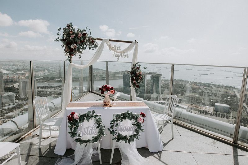 Panoramic view of a modern rooftop wedding setup with white drapes and floral arrangements.