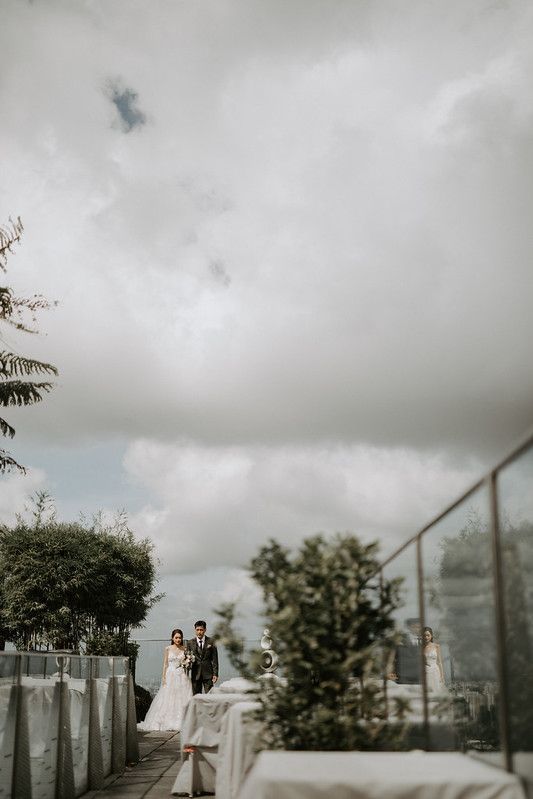 Cloudy day rooftop wedding ceremony with white fabric decorations and glass railings.