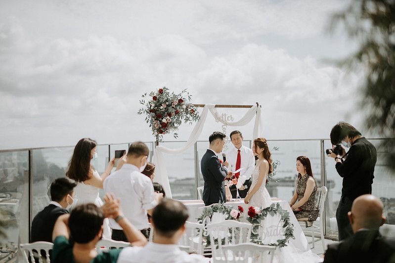 Wedding ceremony setup on a rooftop terrace with white arch and red floral arrangements.