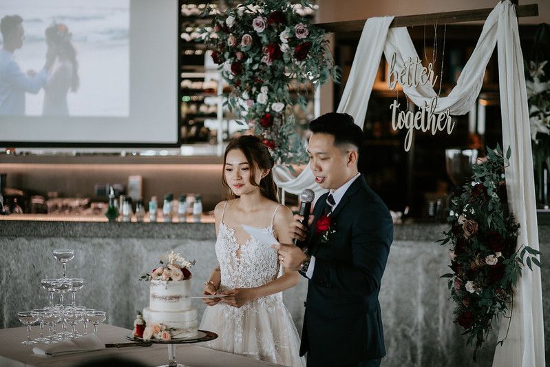 Wedding cake cutting ceremony with elegant white tiered cake and floral decorations.