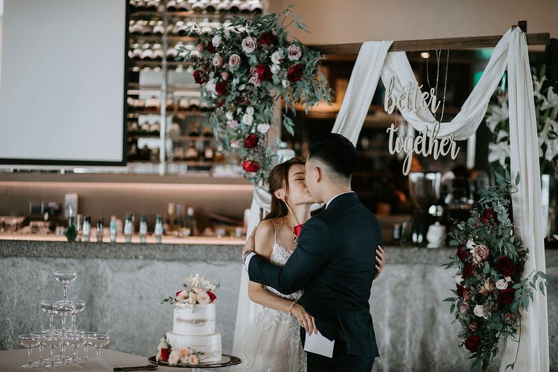 Wedding cake display with white draping and floral decorations in modern venue setting.