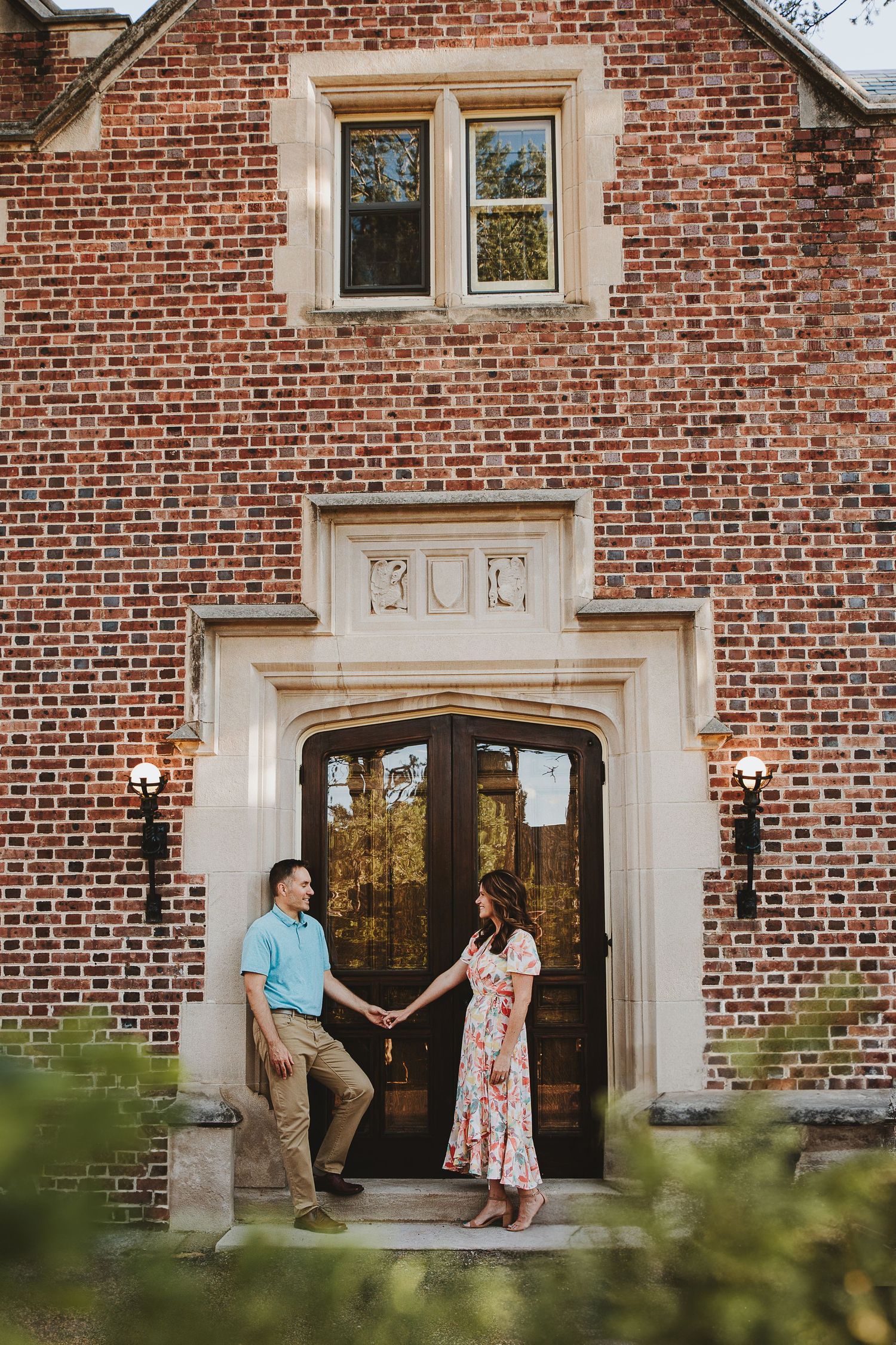 A couple poses at an elegant brick building entrance with classic architectural details.
