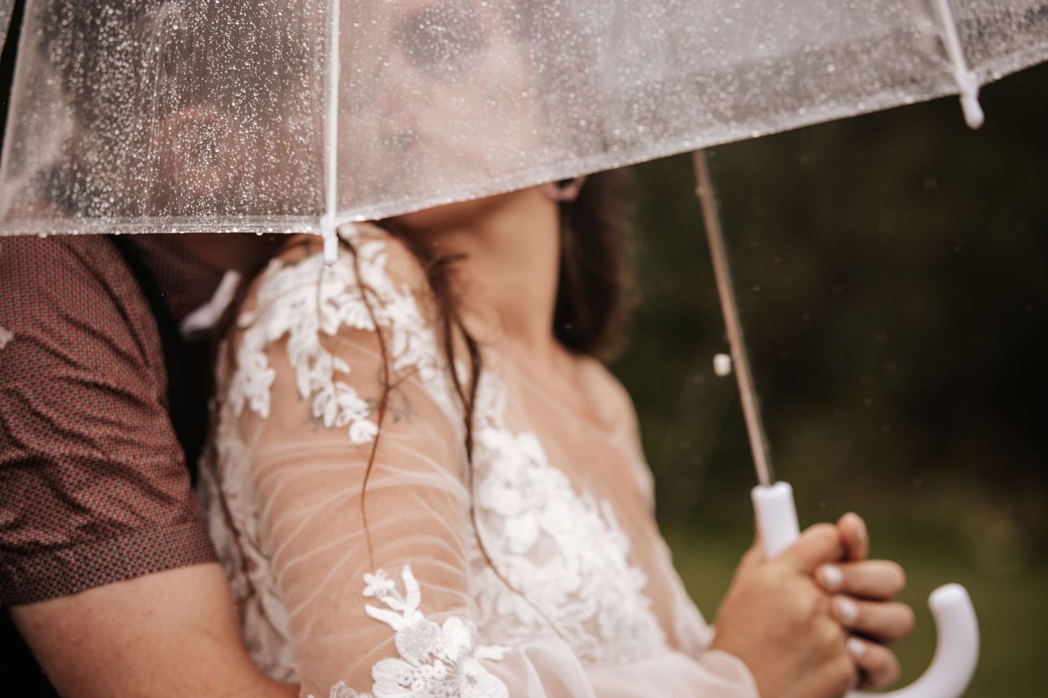 Close-up detail of a lace wedding dress and clear umbrella in natural light.