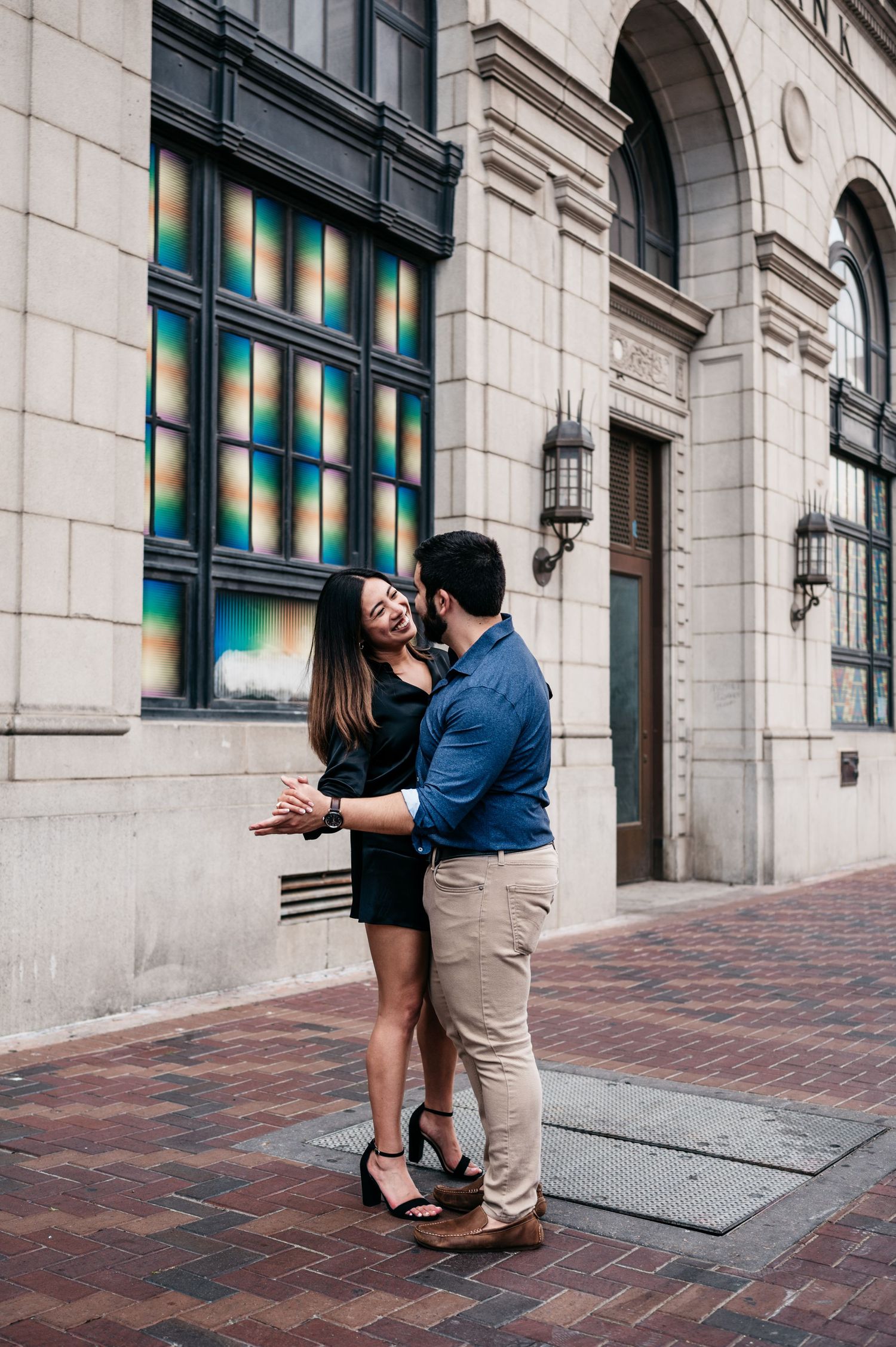 A couple shares an intimate moment against a stone building with colorful stained glass windows.