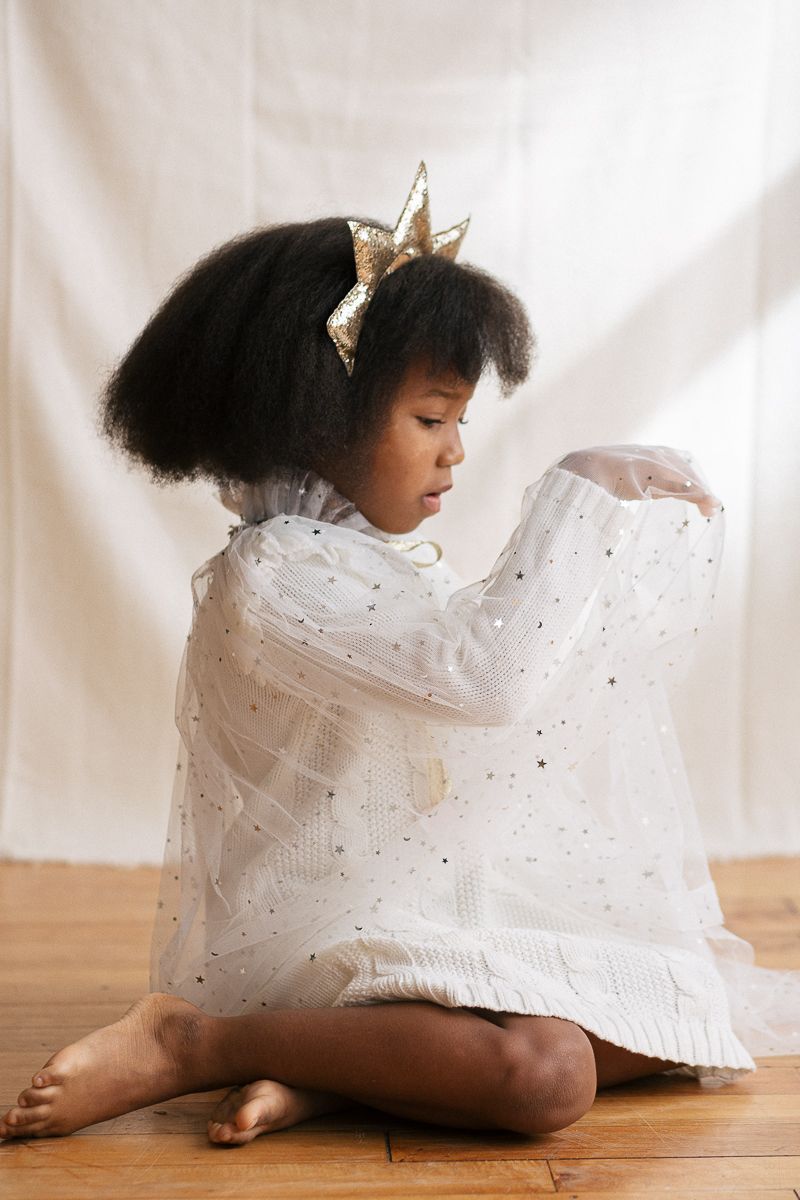 a candid moment of a girl playing with her tule white cape with gold stars during a Holiday session in studio by Paula Brearley