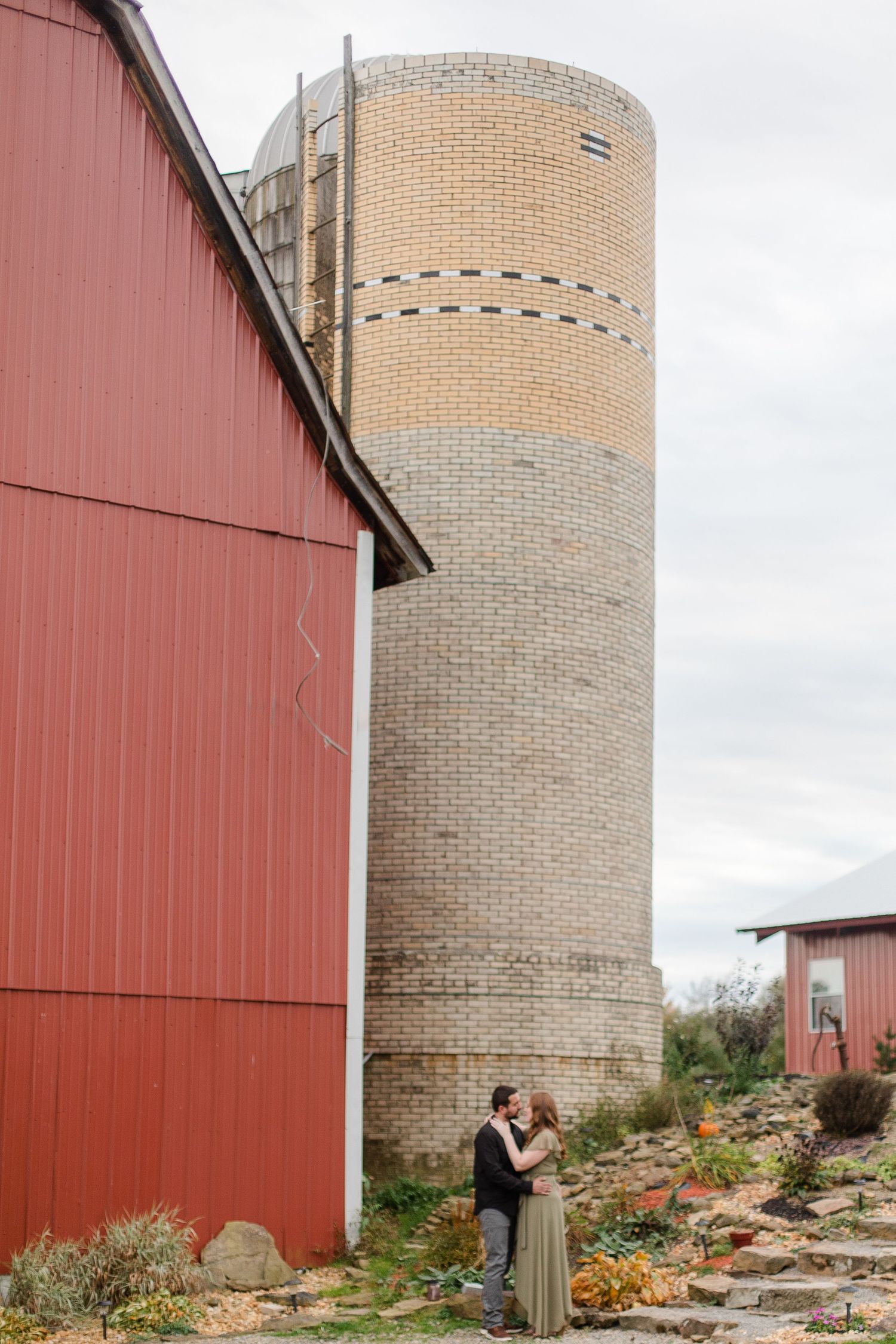 Red barn and cylindrical grain silo against cloudy sky.
