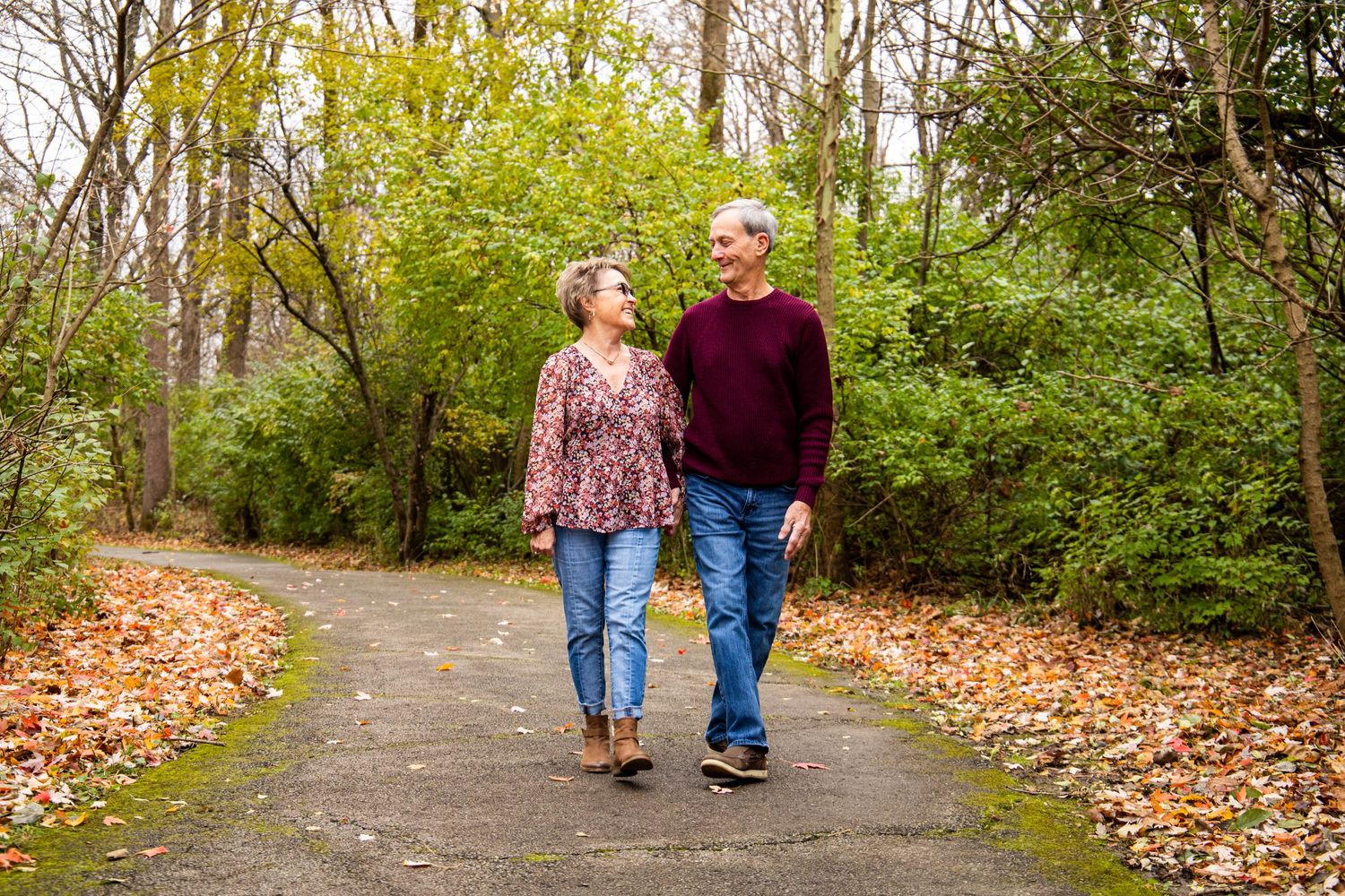 Couple walking together on leaf-covered path during autumn.