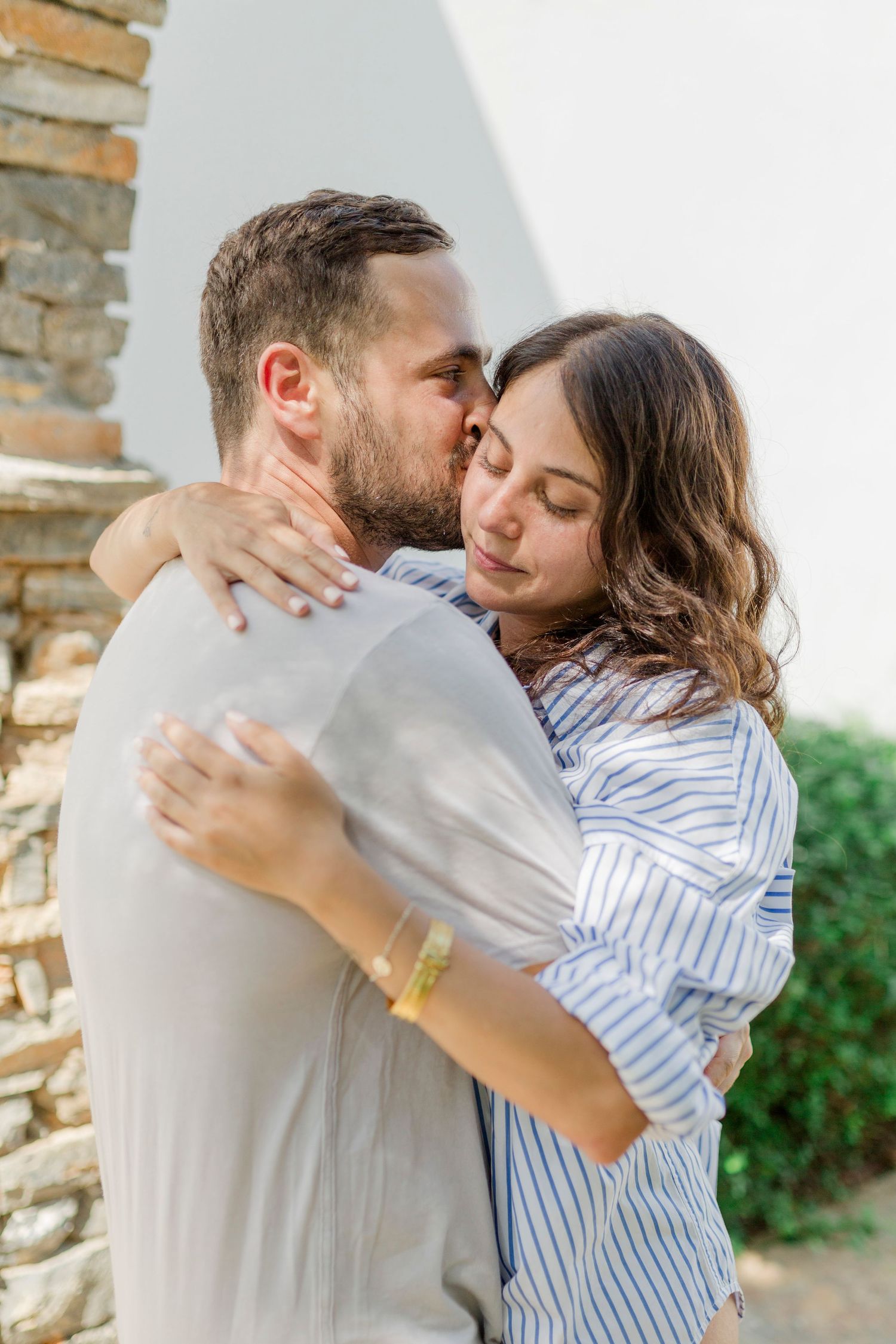 A tender embrace captured between a couple against a stone wall backdrop.