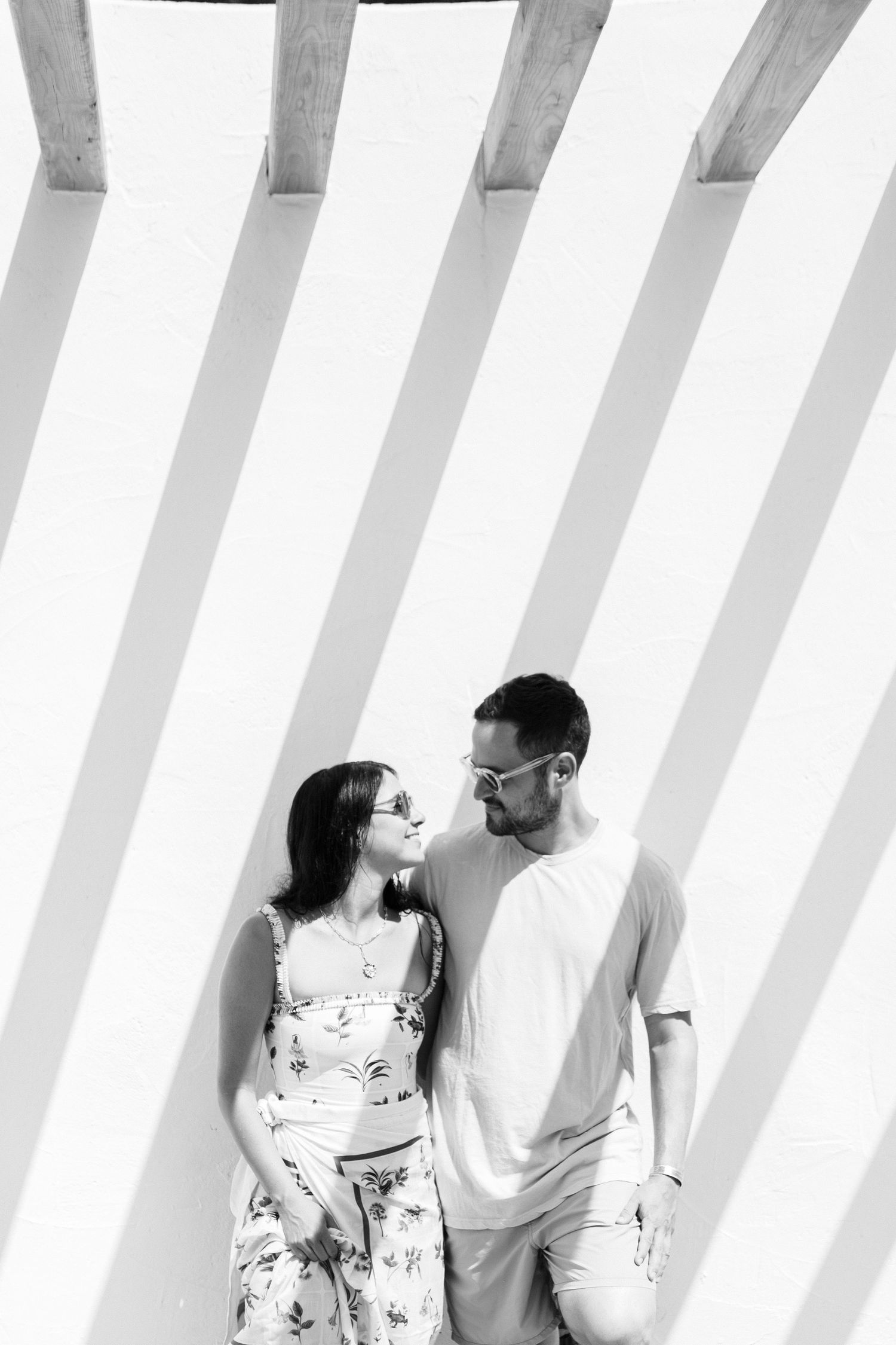 Couple standing in front of white wall with diagonal shadow lines.