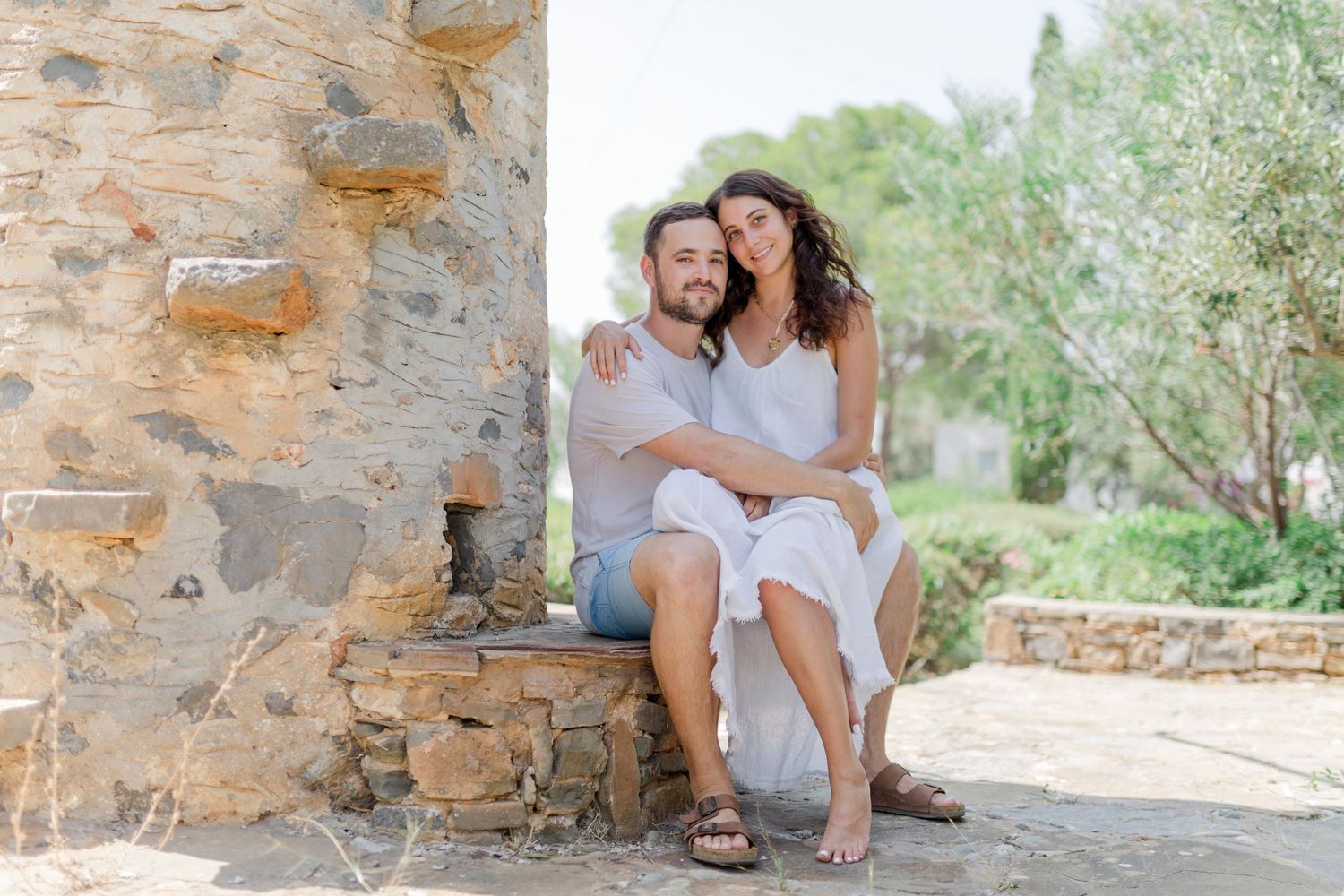 A couple sharing an intimate moment while sitting on stone steps against a rustic wall.