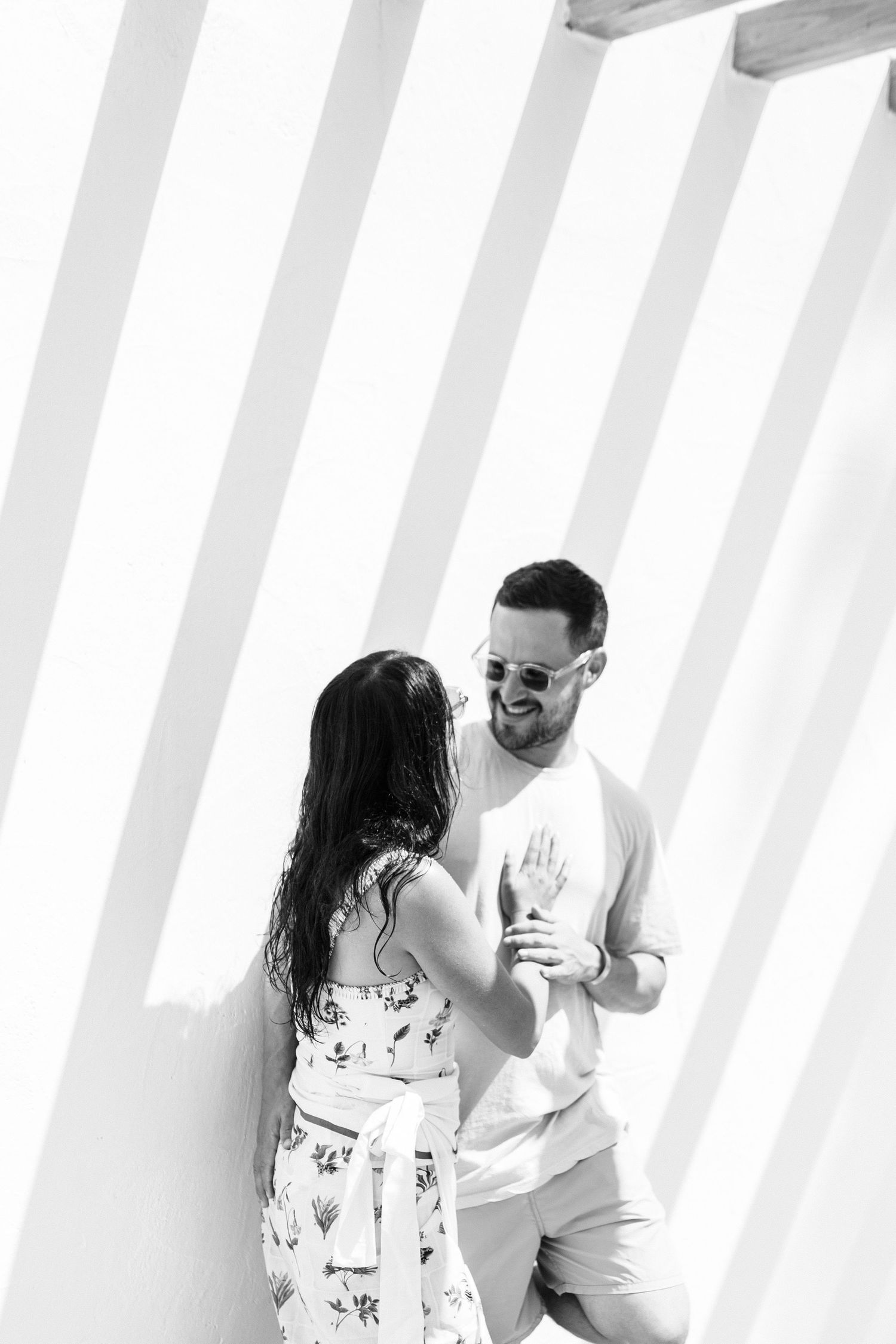 Couple standing in front of white striped wall with shadows.