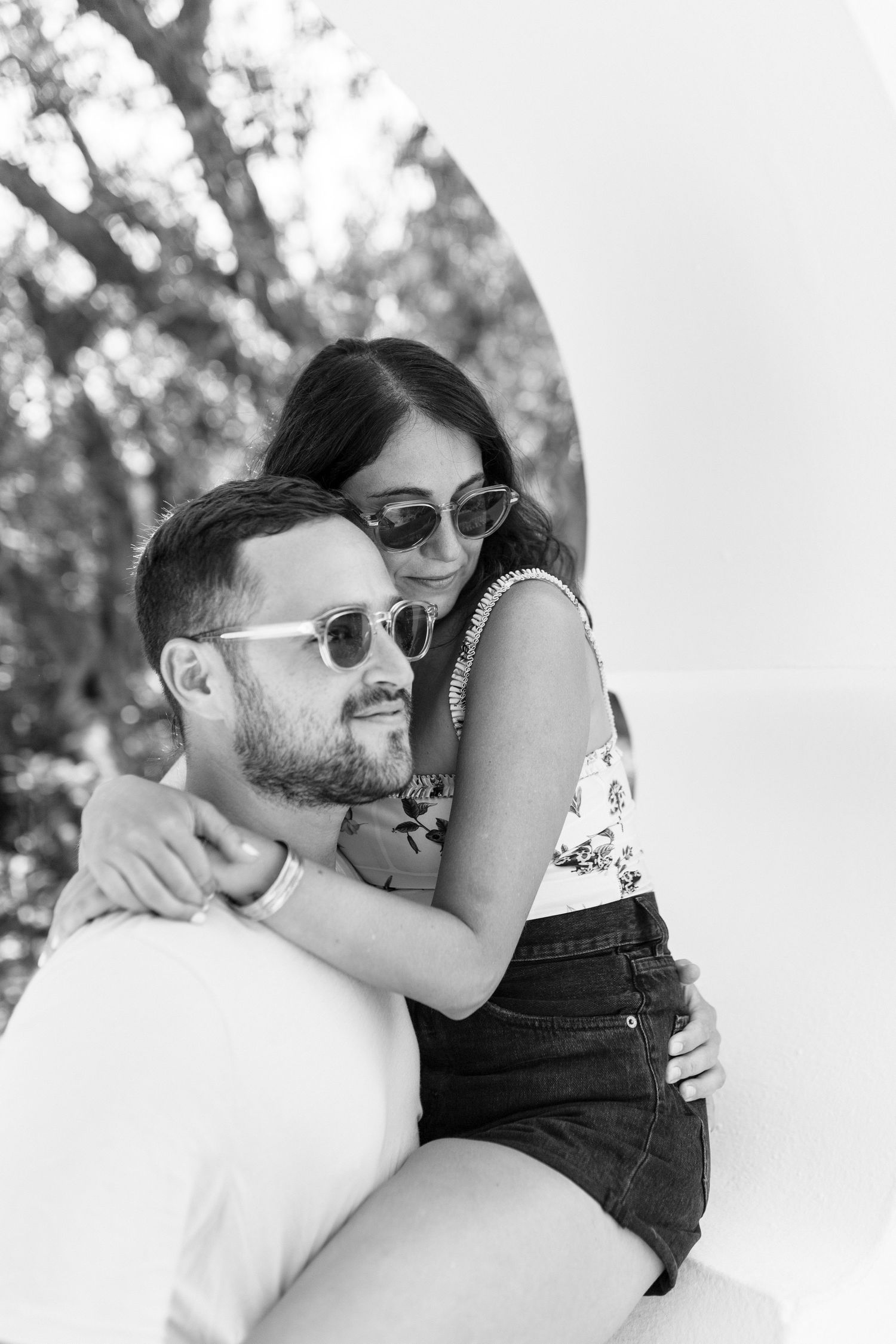 A couple embraces while wearing sunglasses, with trees visible in the background.