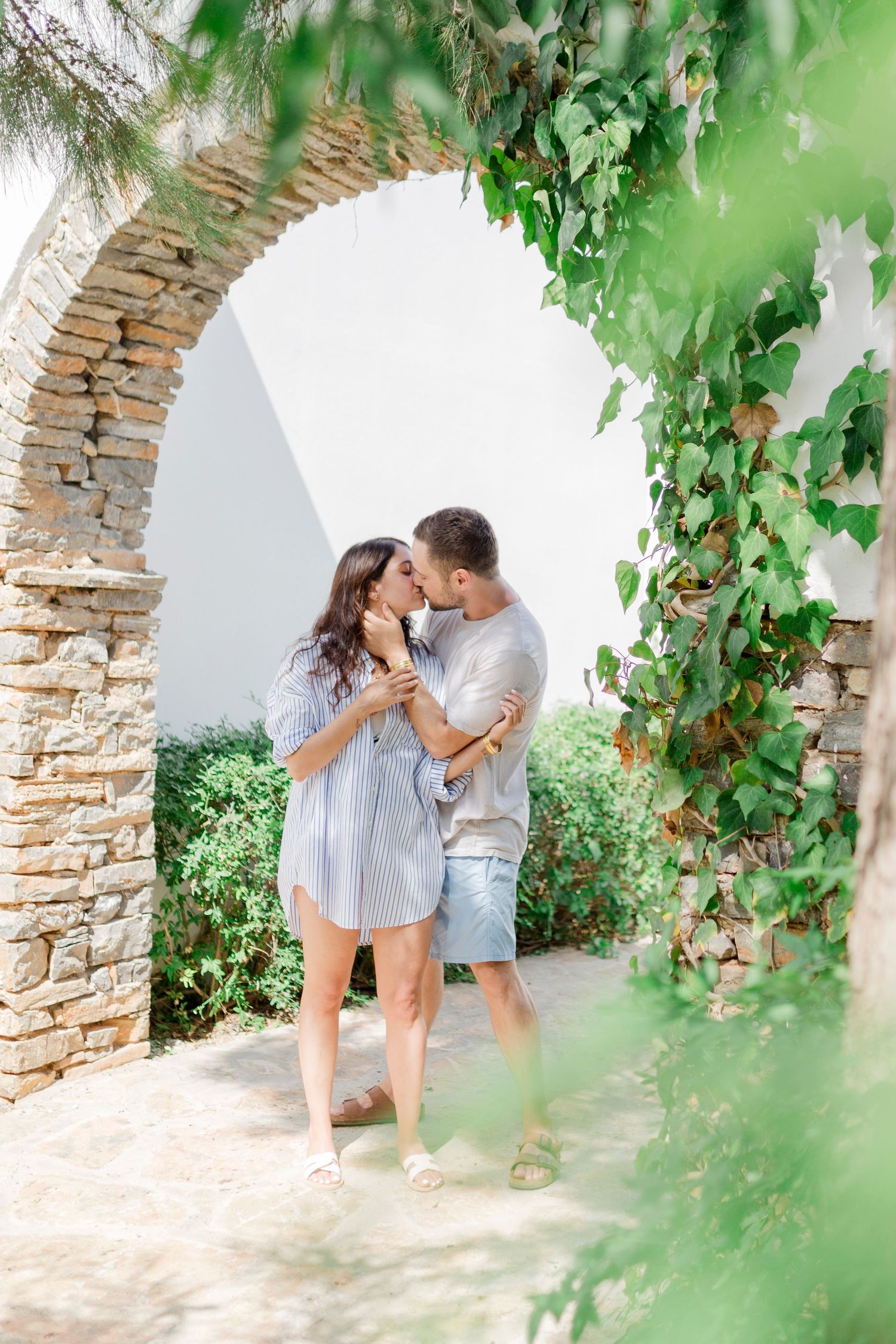 A romantic moment shared under a stone archway covered with green vines.