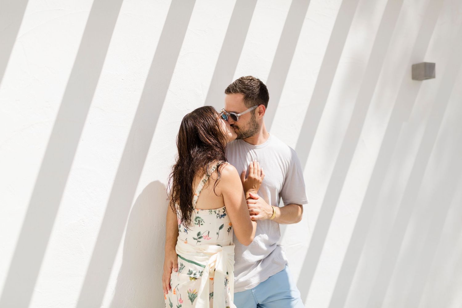 Couple embracing against white wall with diagonal shadow lines.