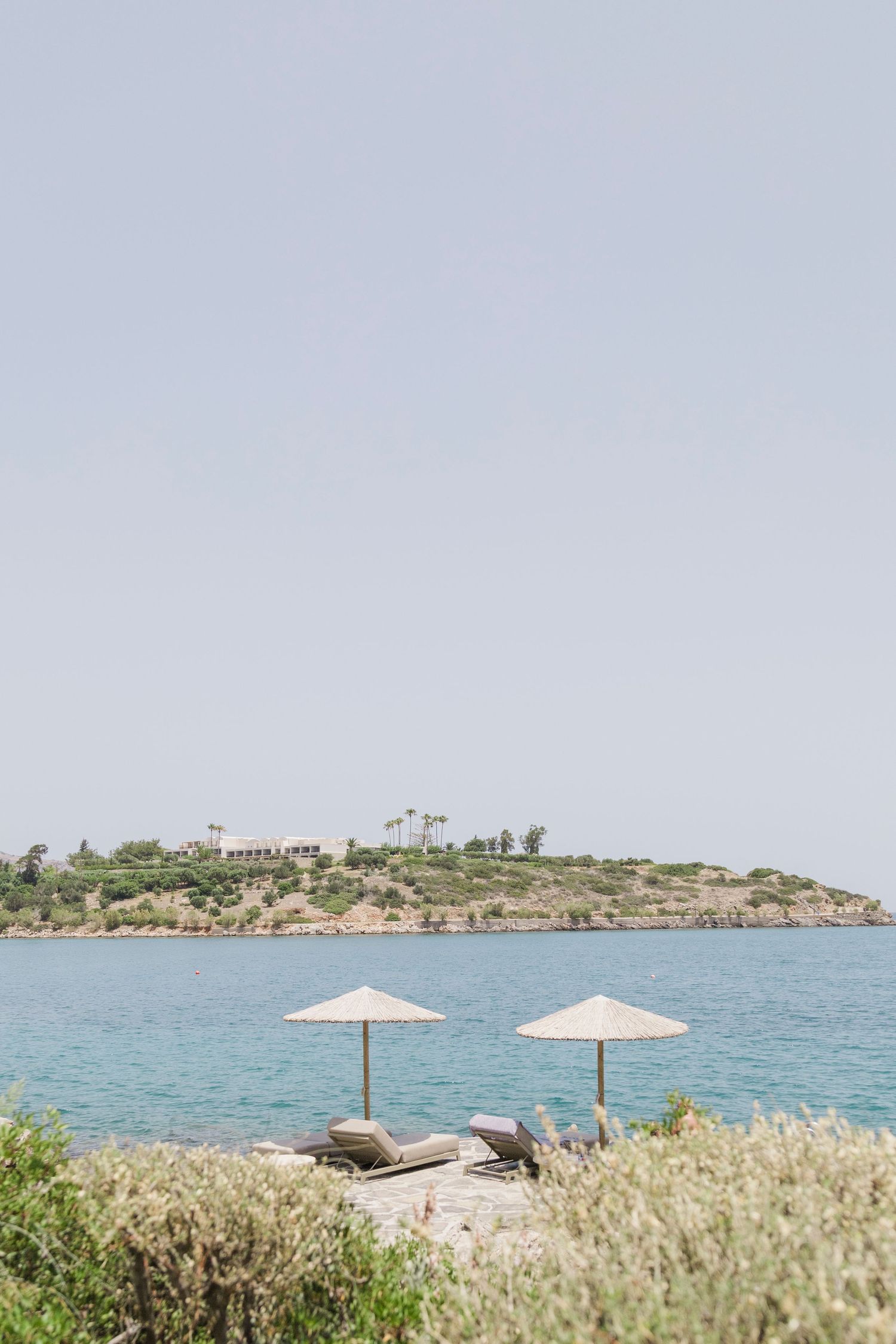 Beach umbrellas on rocky shore with blue sea and island in background.