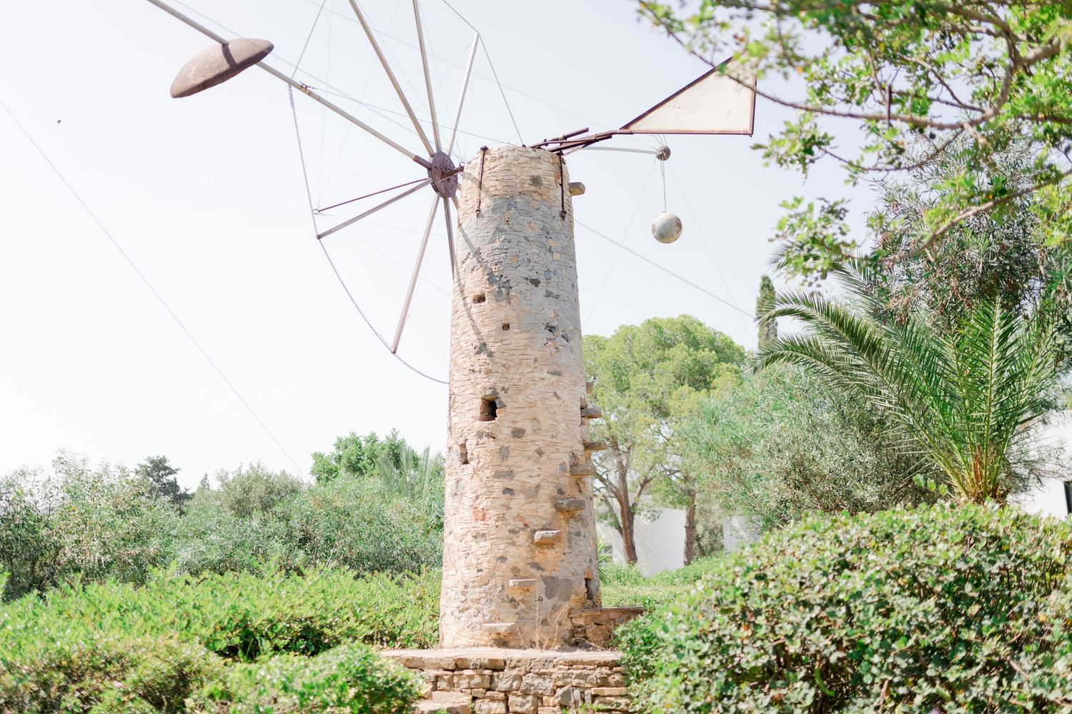 An old Mediterranean stone windmill tower against a bright blue sky with palm trees.