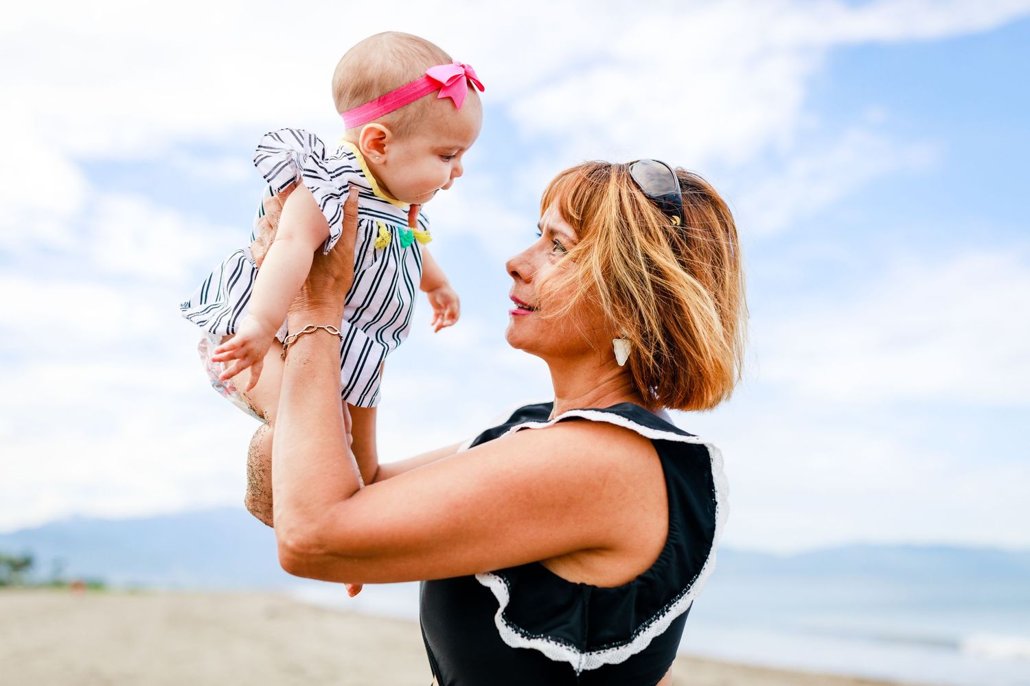 Mother lifting baby in colorful summer outfit at the beach.