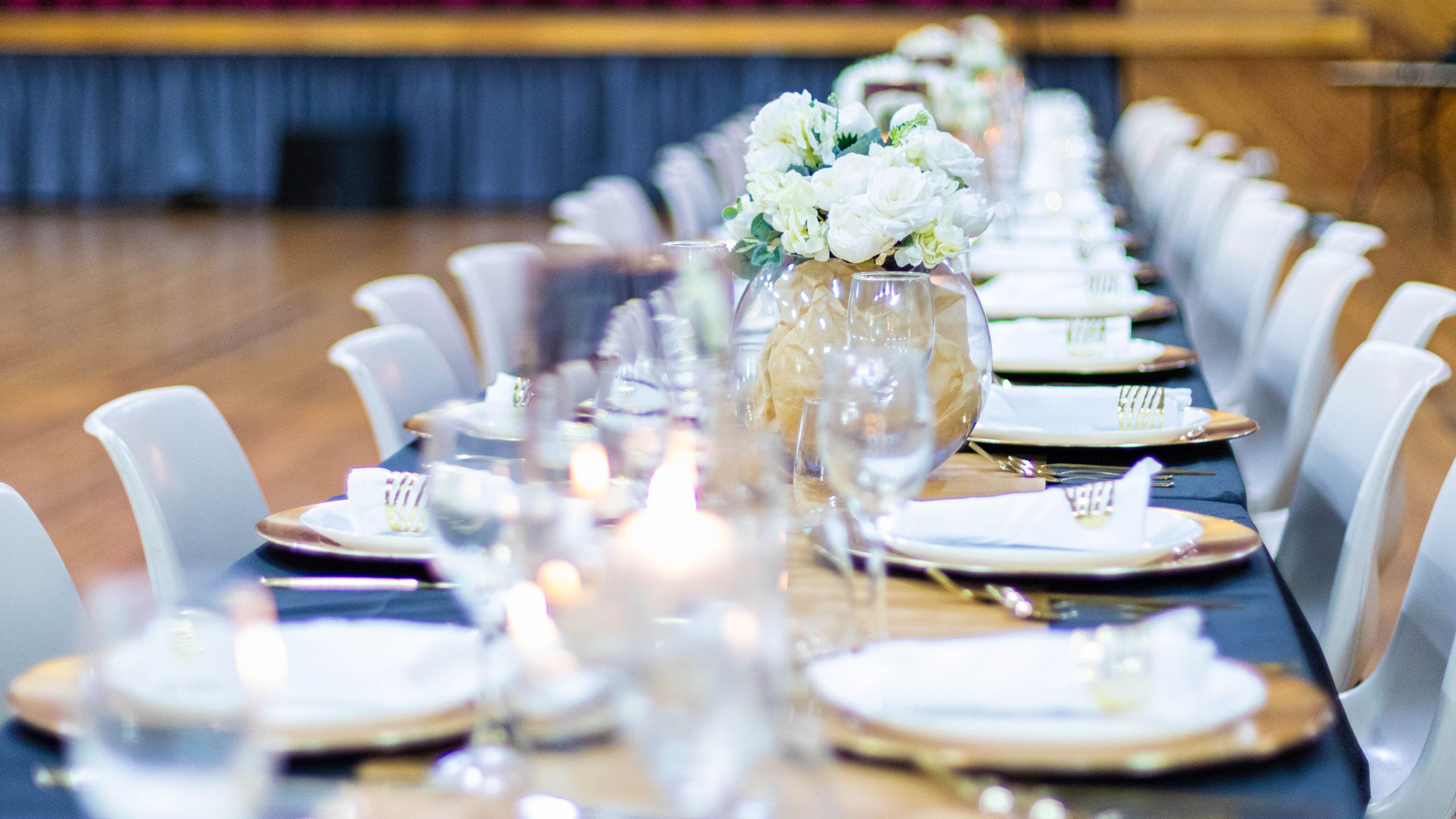 Elegant table setting with white plates, navy napkins and floral centerpieces.