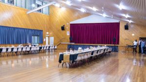 Long banquet tables arranged in a gymnasium with burgundy curtains and wooden floors.