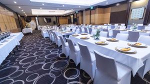 Formal banquet hall setup with white tablecloths and chair covers in a carpeted room.