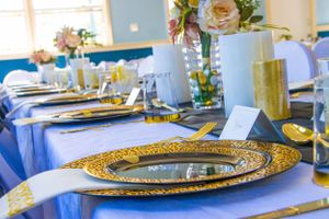 Close-up of formal table setting with gold charger plate and blue tablecloth.